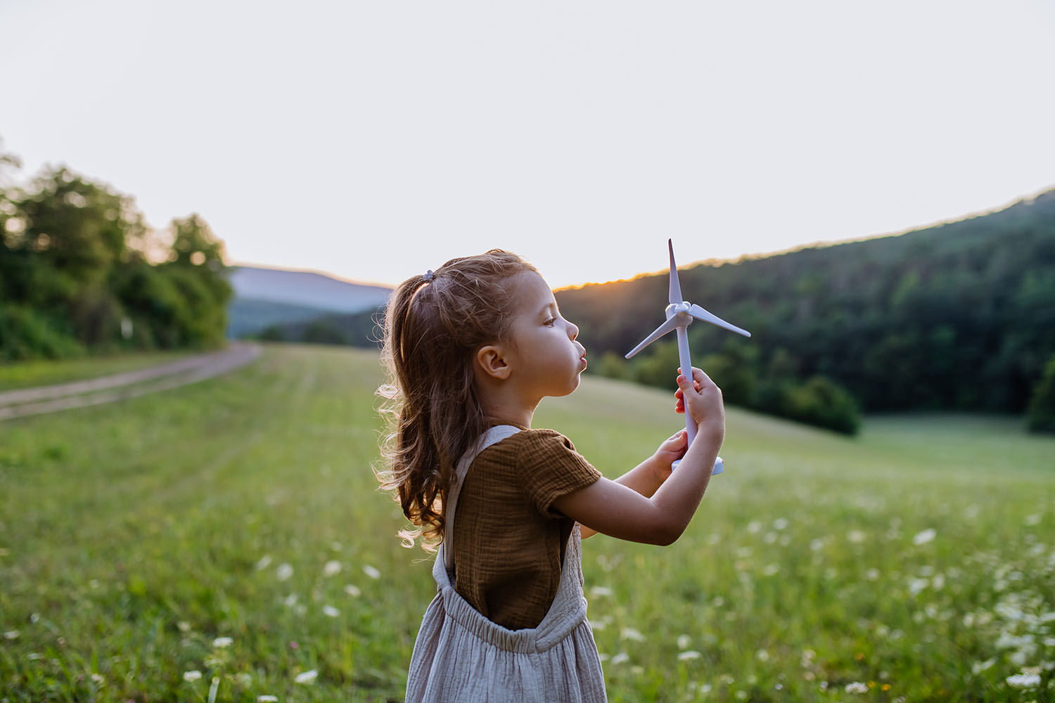 A little girl standing in nature with model of wind turbine. Concept of ecology future and renewable resources.